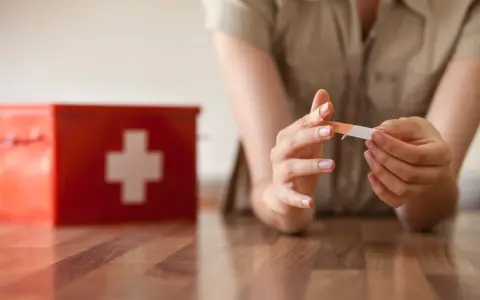 Une personne applique un pansement sur son doigt, près d'une trousse de secours rouge. L'objectif est une cicatrisation rapide.