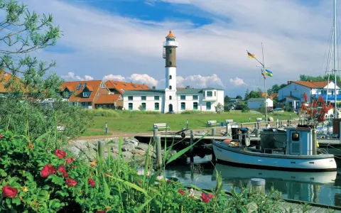 Idyllischer Hafen mit Leuchtturm auf Insel Poel, ein echter Geheimtipp. Boote liegen im Wasser, rote Rosen blühen.