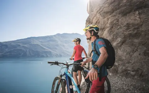 Ein Paar genießt die Aussicht auf den Gardasee während einer E-Bike-Tour. Die Berge und das klare Wasser bilden eine atemberaubende Kulisse.