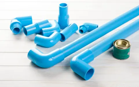 Ensemble de tuyaux et raccords bleus en PVC, prêts pour une installation. Un pot de colle est à proximité.