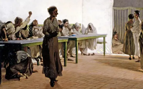 La sala delle agitate: donne in abiti lunghi, alcune sedute ai tavoli, altre in piedi, mostrano espressioni di angoscia e agitazione.