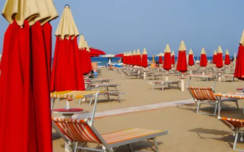 Filetto di ombrelloni rossi e lettini pronti per accogliere i bagnanti sulla costa di Rimini.