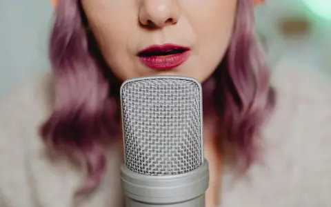 Kobieta z fioletowymi włosami mówi do mikrofonu, jej usta są lekko uchylone, co podkreśla jej tembr głosu.