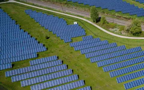 Große Solaranlage auf einer grünen Wiese mit Gleisen im Hintergrund.