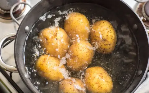 Mehrere ganze Kartoffeln kochen in einem Topf mit sprudelndem Wasser auf dem Herd.