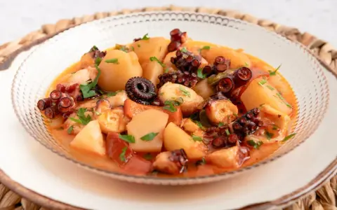 Un delicioso pulpo a la mugardesa, con patatas tiernas y un sofrito sabroso, adornado con perejil fresco.