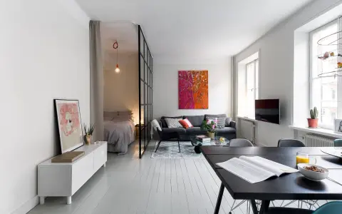 Smart lösning för att bo på liten yta. Sovrummet avskiljs med en glasvägg. Vardagsrummet har en soffa och ett soffbord.
