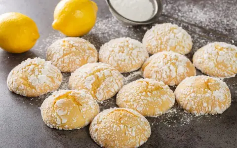 Deliziosi biscotti al limone spolverati di zucchero a velo, con limoni freschi sullo sfondo.