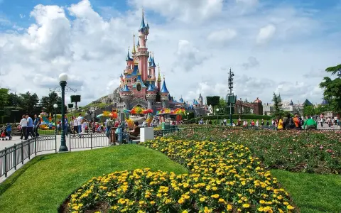 Disneyland Paris castle with colorful flowers and crowds of people.