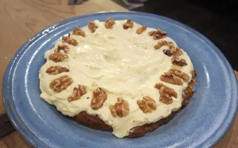 En saftig glutenfri morotskaka med krämig frosting och valnötter på en blå tallrik.