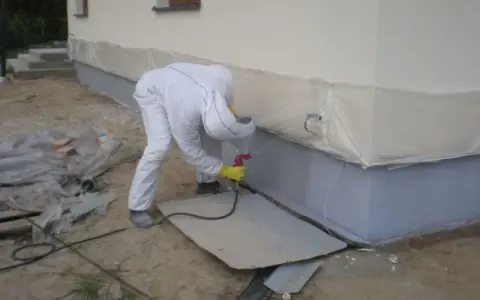 Pracownik w białym kombinezonie maluje fundamenty na kolor przypominający rubinowy.
