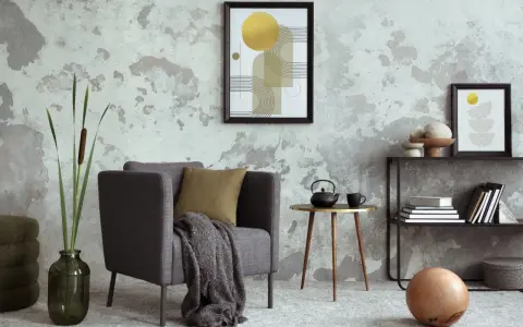 Salón moderno con pared texturizada que combina papel pintado y pintura. Sillón gris, mesa auxiliar dorada, estantería y arte abstracto.