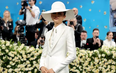 Zendaya, deslumbrante con traje blanco y sombrero, posa ante cámaras y flores.