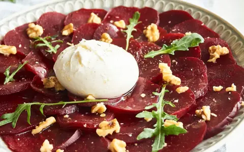 Rote Bete Carpaccio mit Burrata, Walnüssen und Rucola auf einem Teller.