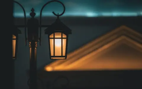 Ciepłe światło zabytkowych lamp miejskich rozświetla zmierzch, rzucając geometryczne cienie na budynek.