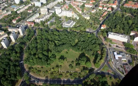 Widok z lotu ptaka na zielony park otoczony drogami, z budynkami mieszkalnymi w tle. To największe rondo w Polsce, które otacza serce miasta.