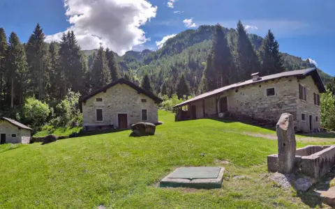 Agriturismi lombardia montagna: casette in pietra immerse nel verde, con boschi e montagne sullo sfondo.
