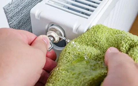 Odkręcanie odpowietrznika grzejnika, gdy jest zimny na dole. Woda kapie na zieloną ściereczkę.