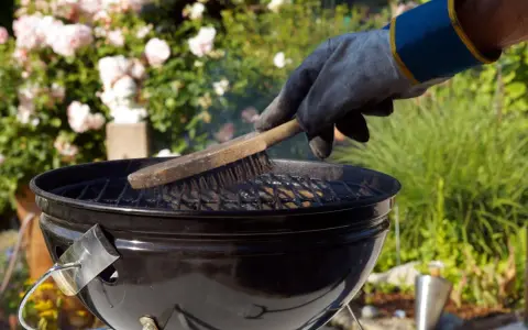 Mit einem Handschuh wird der Grillrost gereinigt. Rauch steigt auf, während die Bürste über die Roste fährt.