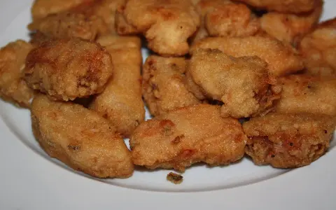 Un plato blanco lleno de trozos dorados y crujientes de japuta en adobo, listos para disfrutar.