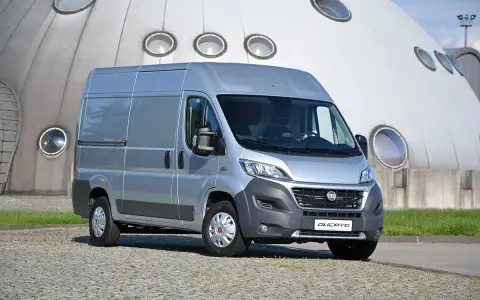 Srebrny Fiat Ducato 2.3 Multijet zaparkowany przed futurystycznym budynkiem z okrągłymi oknami.
