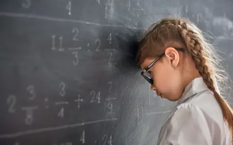 Mädchen mit Brille lehnt frustriert am Tafelbild mit Matheaufgaben. Die note 5 in der schule ist zu viel.