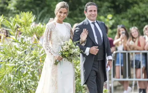 Novia y novio sonríen en la boda de María Pombo. Ella lleva un vestido blanco con encaje y él un traje gris.