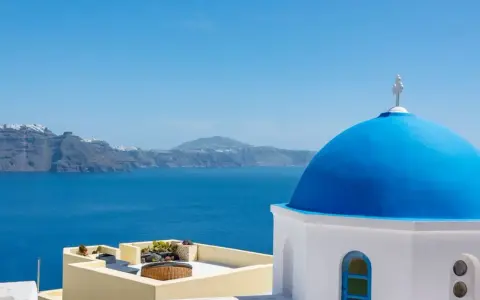 Blaue Kuppel einer Kirche in Oia, Santorini, mit Blick auf das tiefblaue Meer und die zerklüftete Küste.