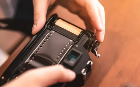 Manos insertando rollo de película en cámara analógica, un paso clave para aprender como revelar fotos en casa.