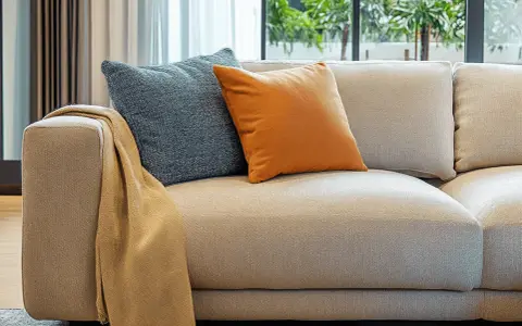 Sofá de tela beige con cojines azul y naranja, y una manta doblada. Ideal para limpiar sofá de tela y mantenerlo como nuevo.