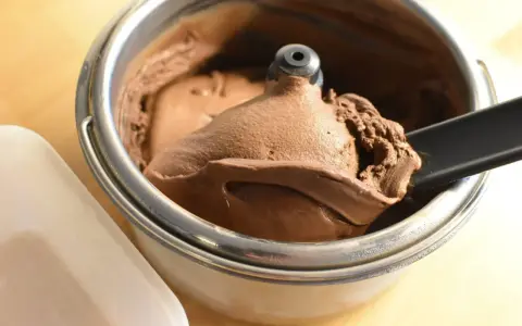 Un cucchiaio nero preleva una porzione di cremoso gelato fatto in casa al cioccolato da una gelatiera.