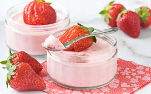 Delicioso postre con fresas, cremoso y ligero, servido en frascos de vidrio. Una fresa fresca corona cada porción.