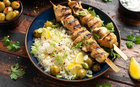 Deliciosos pinchitos de pollo a la parrilla servidos con arroz blanco, aceitunas verdes, rodajas de limón y cebolleta picada.