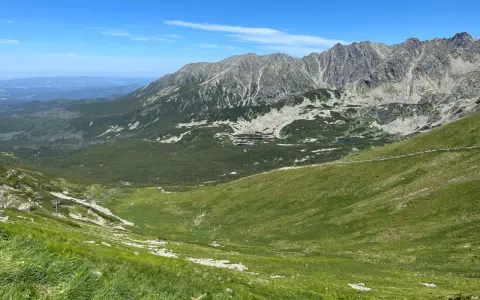 Widok na Tatry z zielonymi zboczami i skalistymi szczytami. W oddali widać budynki. Zastanawiasz się, ile km jest na Kasprowy Wierch?