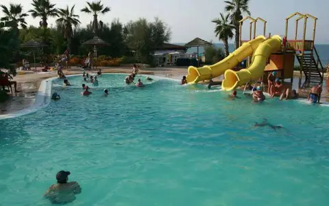 Piscina con scivoli gialli e persone che nuotano, ideale per campeggi puglia sul mare per bambini.