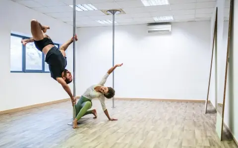 Para ćwiczy pole dance, pokazując efekty odchudzania. On wisi na rurze, ona kuca obok.