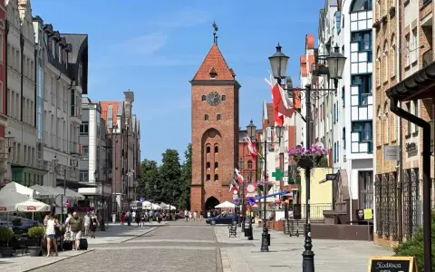 Ulica w Elblągu, z charakterystyczną wieżą i kolorowymi kamienicami. To najniżej położone miasto w Polsce, pełne urokliwych zakątków.