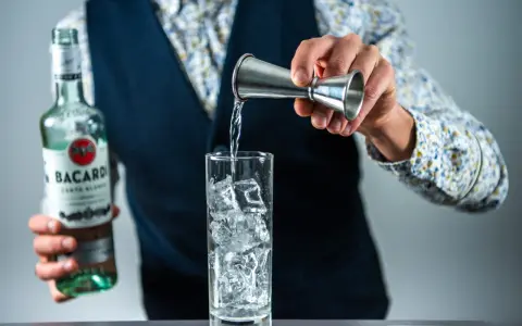 Barman nalewa rum Bacardi do szklanki z lodem, przygotowując Cuba Libre. Jaki rum do drinka? Bacardi Carta Blanca.