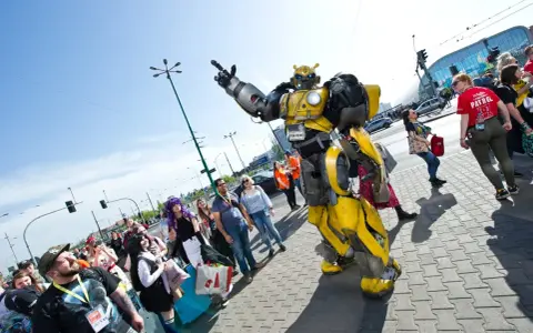 Bumblebee wita fanów na Pyrkonie. Tłum ludzi w kostiumach i z torbami idzie chodnikiem.