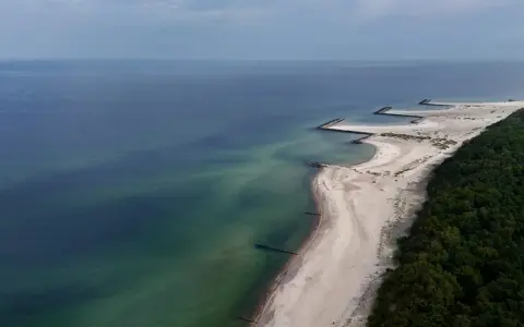 Plaża w Jarosławcu, zwana czasem "plażą dubaj", z kamiennymi falochronami i zielonym lasem.
