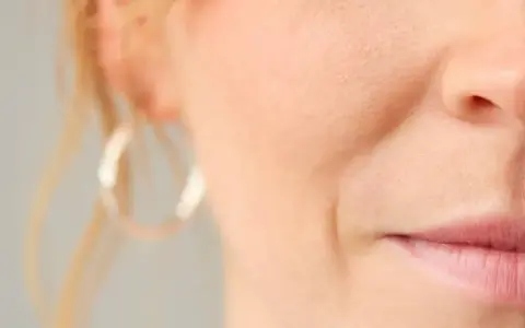 Nahaufnahme eines Gesichts mit sichtbarer Nasolabialfalte, die mit 40 Jahren typisch ist. Eine Frau mit dezentem Lächeln.