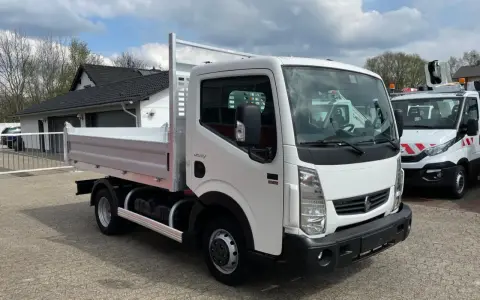 Biały Renault Maxity z otwartą skrzynią ładunkową stoi na placu. W tle budynek i inne pojazdy.