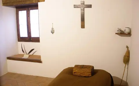 A monk's simple cell, showing where monks sleep: a narrow bed with a wooden block for a pillow, a crucifix, and a window.