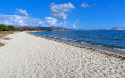 Spiaggia Cala d'Ambra: sabbia dorata, mare azzurro e montagne all'orizzonte. Un angolo di paradiso per rilassarsi.