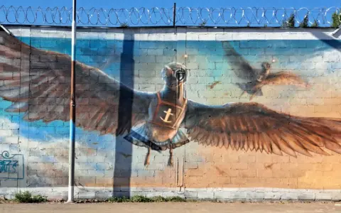 Street art i Stockholm: en stor målad fågel med utbredda vingar, som flyger mot en blå himmel.