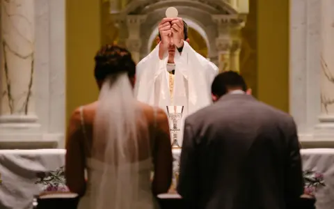 Para młoda klęczy przed ołtarzem, kapłan podnosi hostię. Modlitwa za żonę w tym ważnym dniu.