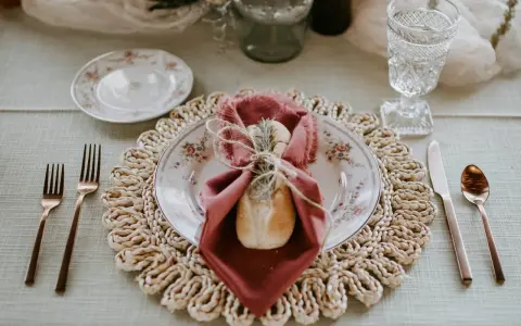 Une table dressée avec élégance, une assiette fleurie, une serviette bordeaux et une **fourchette à la française** en cuivre, prête pour un repas raffiné.