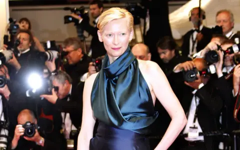 Tilda Swinton poses on the red carpet, surrounded by flashing cameras and eager photographers.