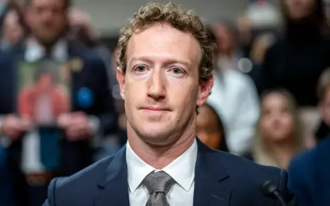 Mark Zuckerberg im Anzug, im Hintergrund unscharfe Menschen und ein Foto.