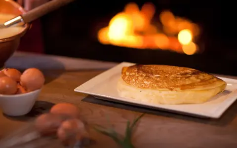 Une omelette mere poulard dorée et moelleuse, prête à être dégustée près d'un feu de cheminée. Des œufs frais sont visibles à côté.